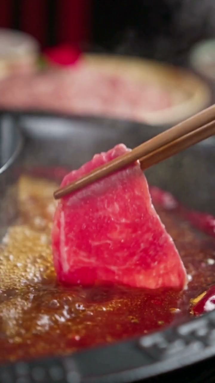 Marbled beef being lowered into bubbling hot-pot broth